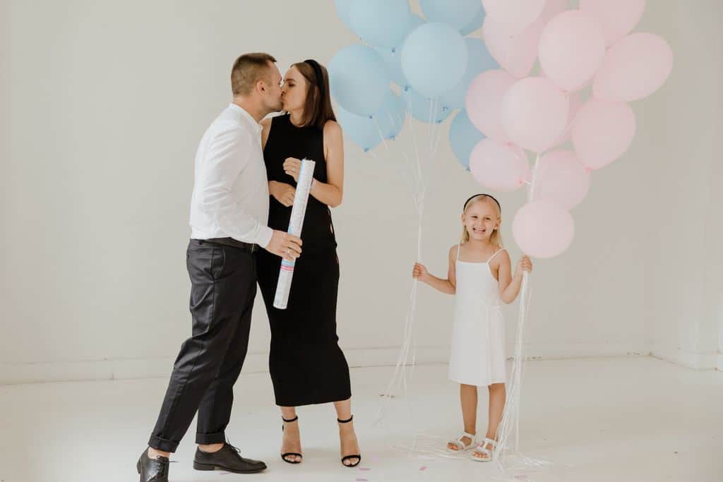 A joyful family celebrating a gender reveal with balloons indoors, featuring parents and a smiling child.