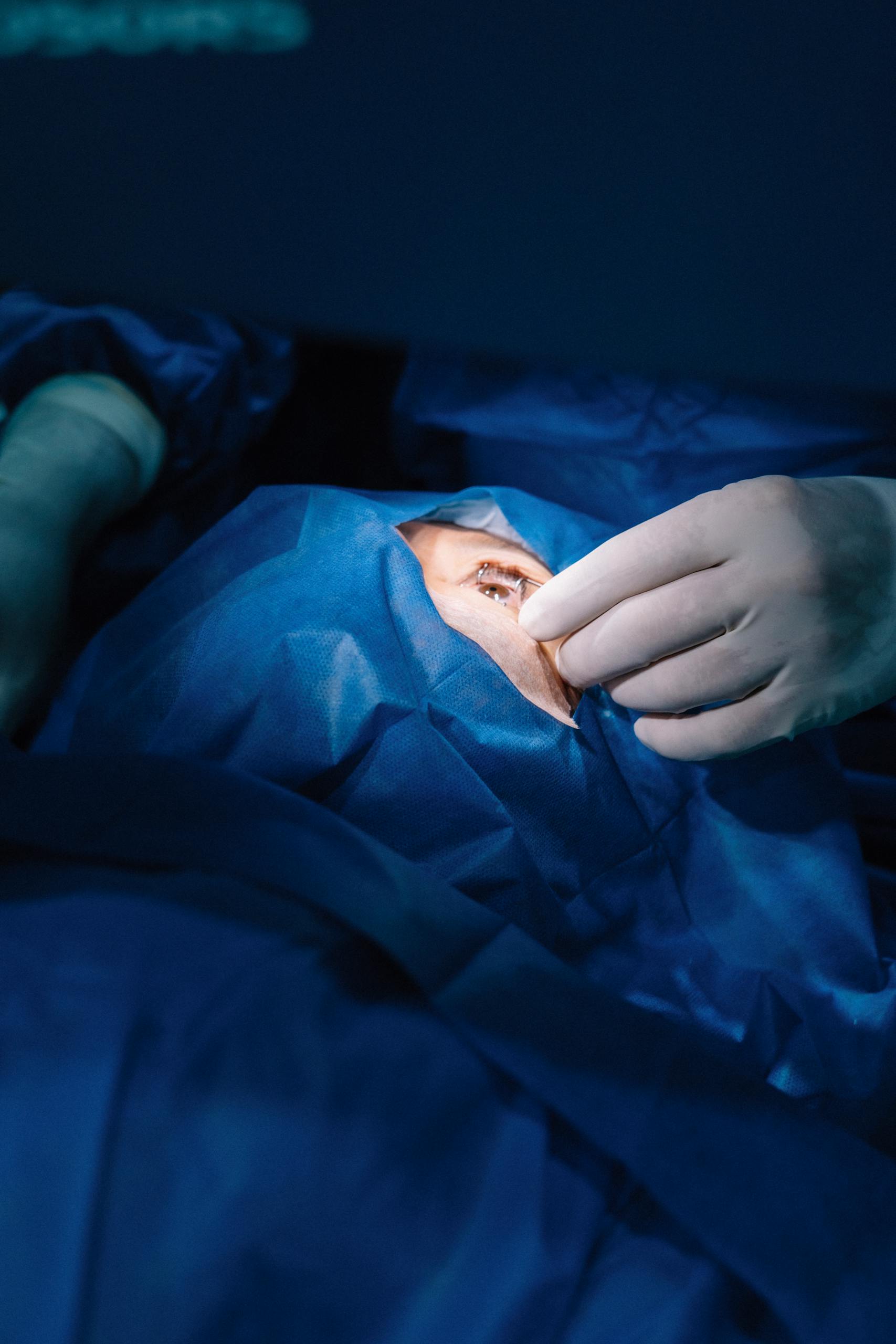 A surgeon's hand performing a procedure on a patient's eye in a sterile operating room environment.